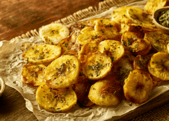 Golden Crispy Baked Green Banana Chips Dusted With Roasted Cumin And Dried Mint On Parchment And Rustic Wood