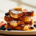 Golden Brown French Toast Stack Dusted With Powdered Sugar, Fresh Berries, And Maple Syrup On A White Plate