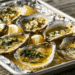 Six Baked Oysters On Half Shells With Golden Garlic Butter And Parsley On A Foil-Lined Baking Sheet