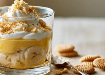 Layered Banana Cream Pudding In A Clear Glass With Custard, Banana Slices, Whipped Cream, And Crushed Wafers