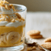 Layered Banana Cream Pudding In A Clear Glass With Custard, Banana Slices, Whipped Cream, And Crushed Wafers