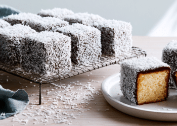 Coconut-Coated Chocolate Lamingtons On A Wire Rack And White Plate, One Halved Showing Golden Sponge Inside