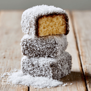 Classic Australian Lamington Recipe For A Delicious Dessert - Thefoodiebunch Coconut-Coated Chocolate Lamingtons On A Wire Rack And White Plate, One Halved Showing Golden Sponge Inside