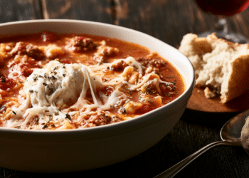 Lasagna Soup With Ground Beef, Fusilli, Ricotta Dollop, And Melted Mozzarella In A White Bowl